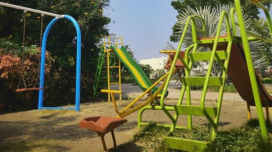 An image of a park with a slide, a see saw, and a pair of swings with greenery around