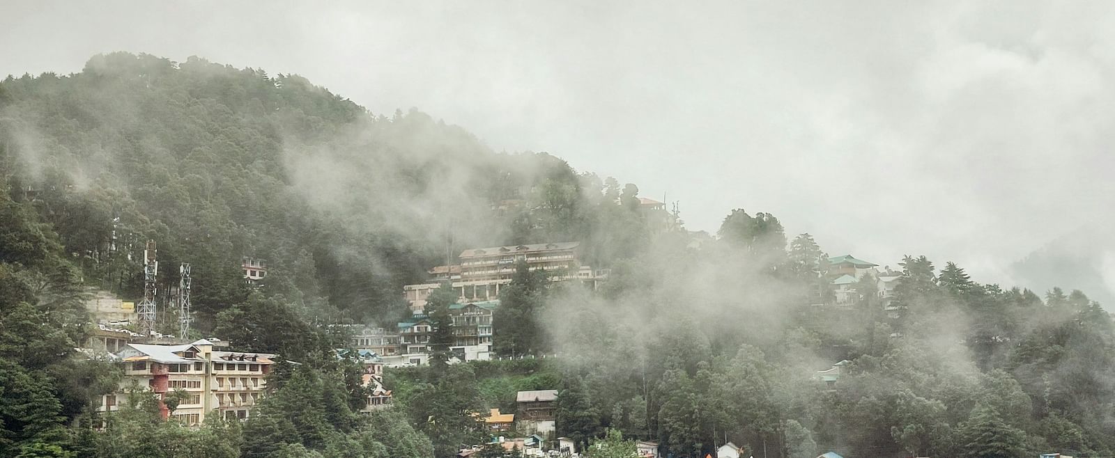 A hillside covered in mist-shrouded houses and dense green forest, suggesting a mountain town on a foggy morning.