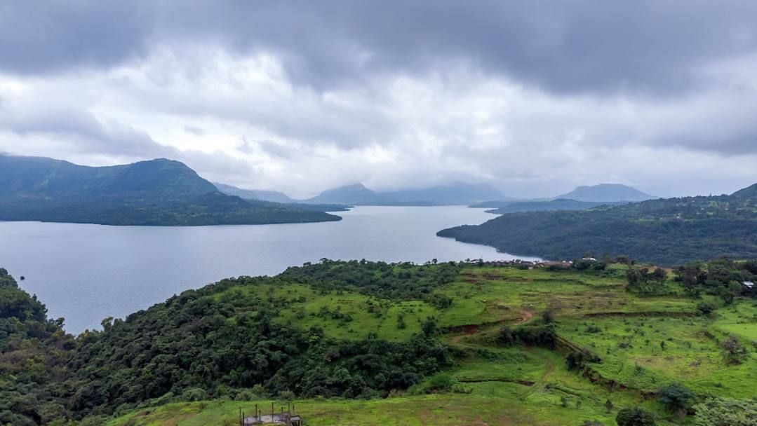 Elevated view of a lush green valley and lake with mountains in the distance.