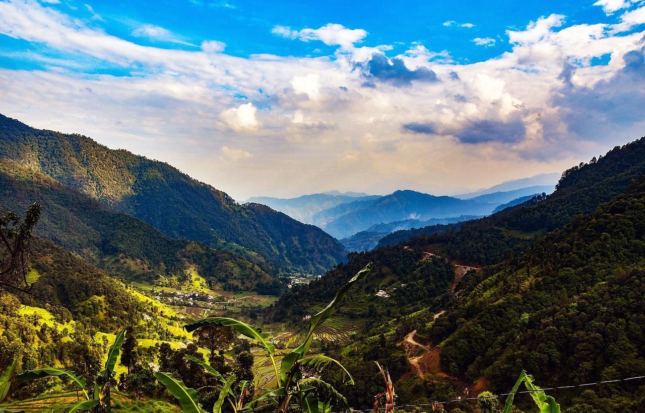 An image of a scenery with mountains, grass, and clouds  