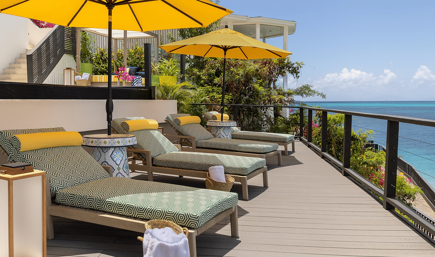 A rooftop deck with lounge chairs and yellow umbrellas overlooks a calm ocean under a clear sky.