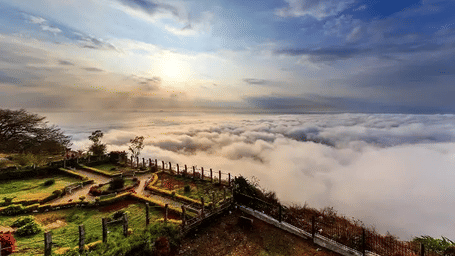 A panoramic shot of Nandi Hills in Bengaluru featuring amnucured garden overlooking a cloud covered landscape.