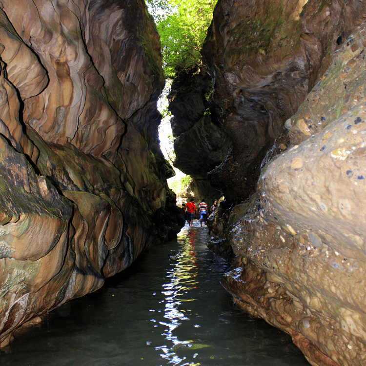 A shallow waterbody body moving through the opening in between two rock formations at Robber's Cave, and people walking in the distance—One of the best Dehradun sightseeing places.