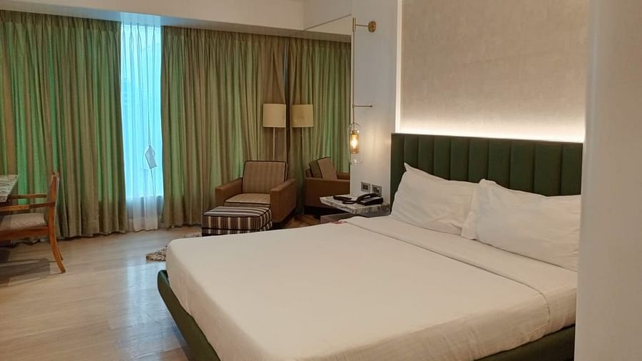 A warmly lit executive room in Mirage Hotel, featuring a king size bed, a lounge chair, a work desk, and a wall to wall window with partially open drapes.