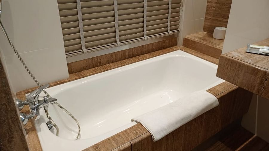 A modern bathroom in an executive room at Mirage Hotel, featuring a white, built-in bathtub, and a wall-mounted hand shower.
