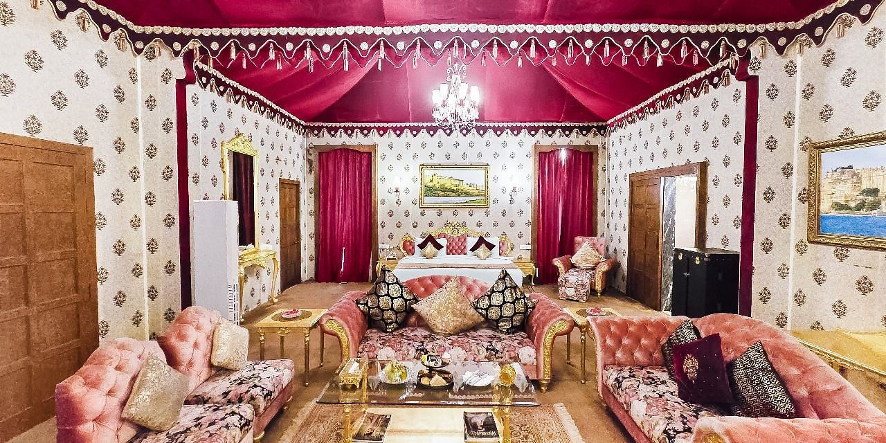 Overview of a  lavishly decorated tent suite at the Rajasthali Resort & Spa in Jaipur features a four-poster bed, ornate furnishings, and a red draped ceiling.