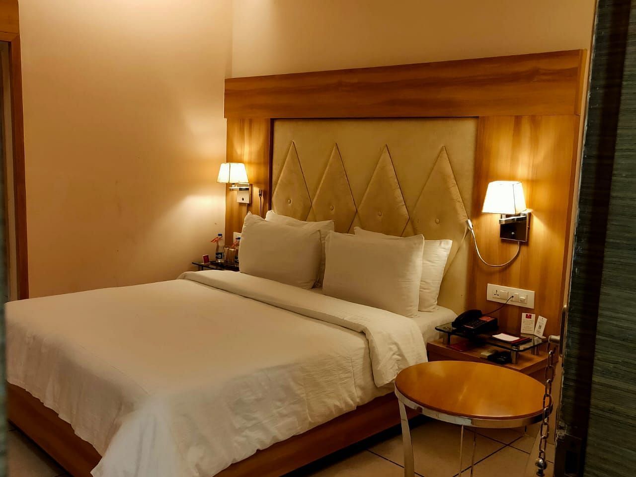 A cosy hotel bedroom  featuring a neatly made bed, bedside lamps, and a decorative headboard - Rang Lords Inn Bharuch