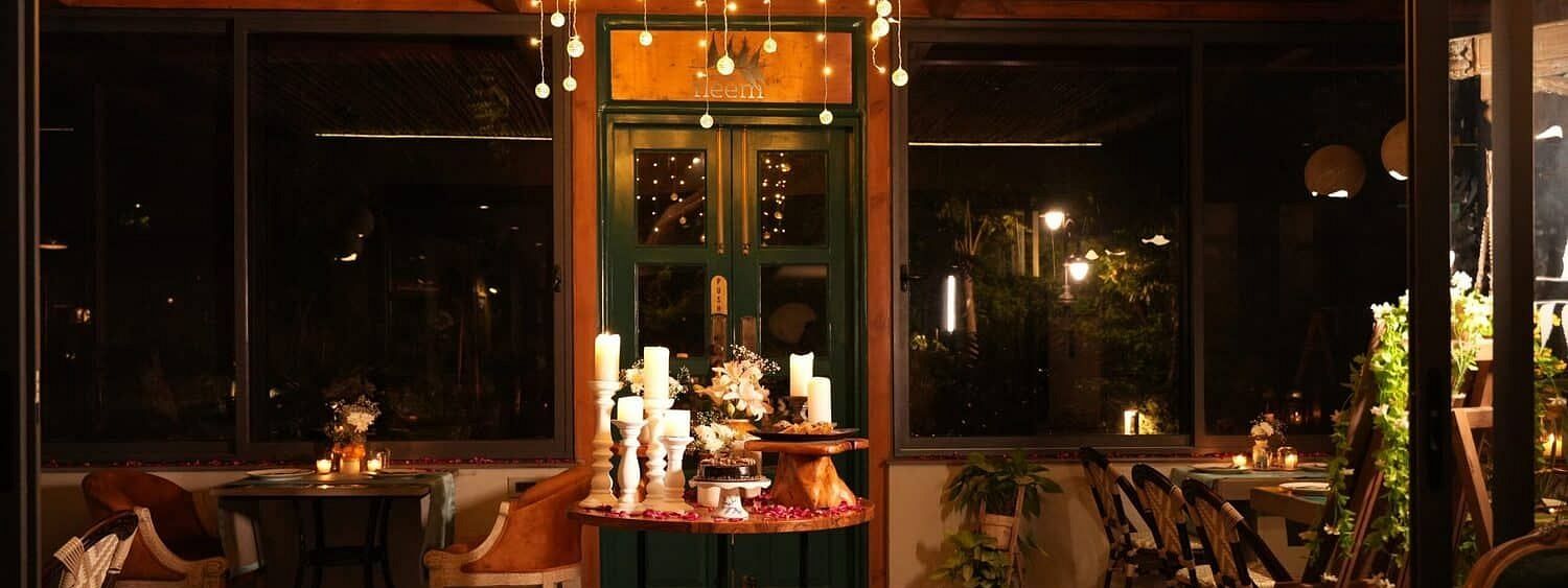 Indoor dining area at Karma Chalets with chandeliers, decorated tables, and large glass windows.