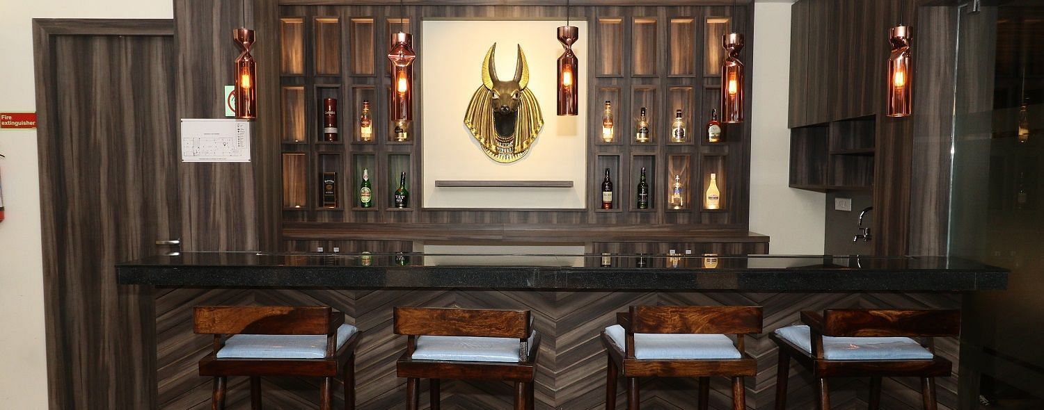 A well-stocked bar area with dark wooden counters, high bar stools, and bottles displayed on shelves, illuminated by hanging lights - Sea Hills Hotels, Sri Vijaya Puram (Port Blair)