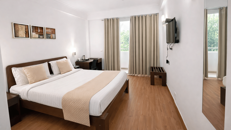 A bedroom featuring a king size bed, bedside tables, wall-mounted television, large windows, and a mirror at EMBLEM - Arjun Marg, Golf Course Road, Gurgaon.