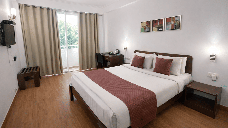 A bedroom featuring a king size bed, bedside table, wall art, wall-mounted television, and balcony at EMBLEM - Arjun Marg, Golf Course Road, Gurgaon.