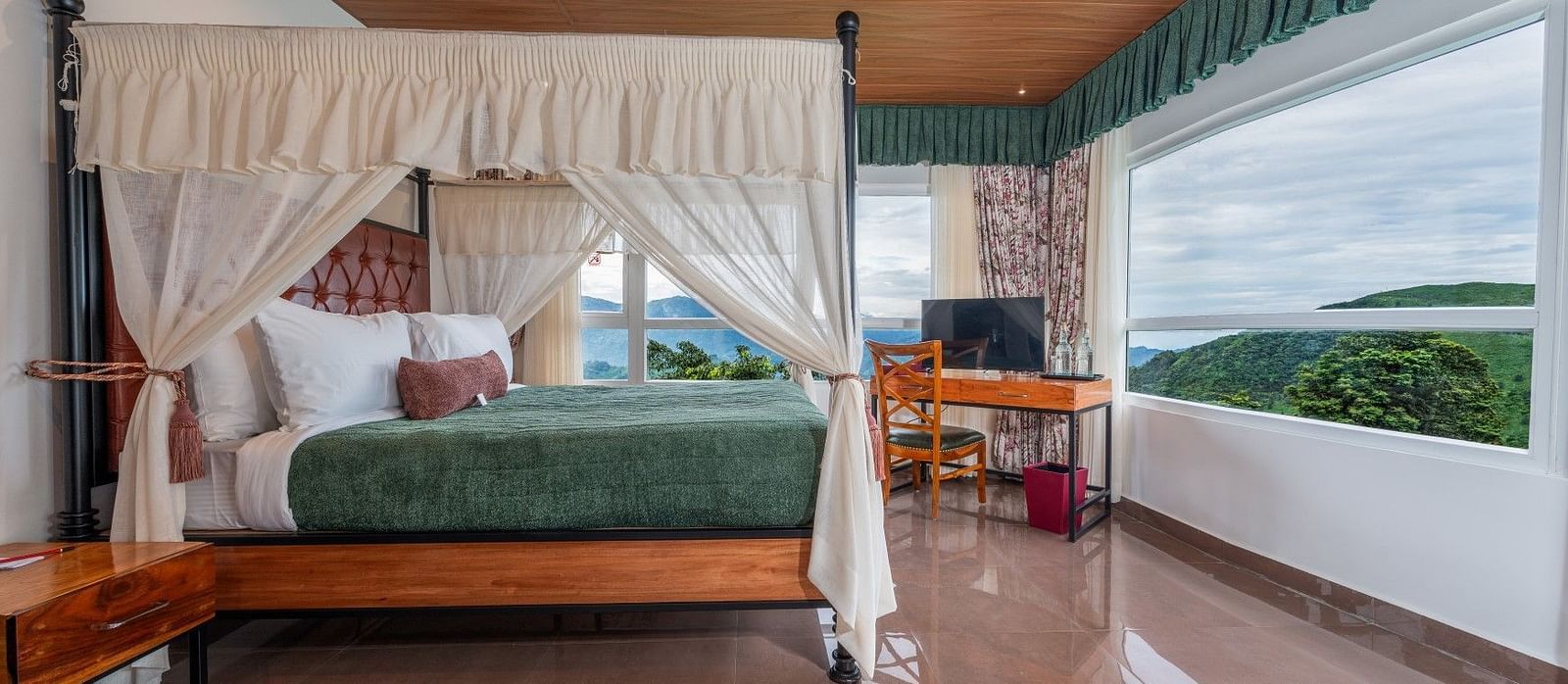  A generously sized bed with curtains on the sides, accompanied by wooden furniture and a breathtaking mountain view through the large windows.