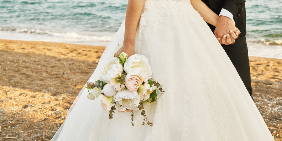 Bride in white wedding gown holding hands with groom at a beach