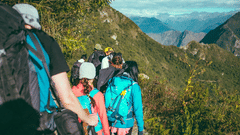 a group of people walking on a trekking trail, going downhill next to a mountain