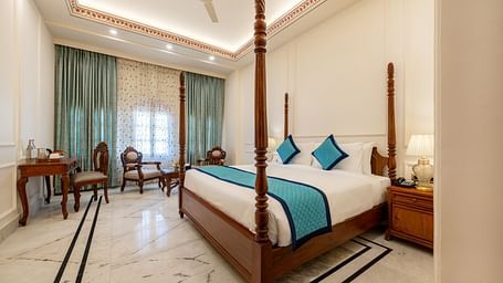 full view image of a room featuring a regal double bed with blue cushions kept over it - Brij Castle, Jaipur
