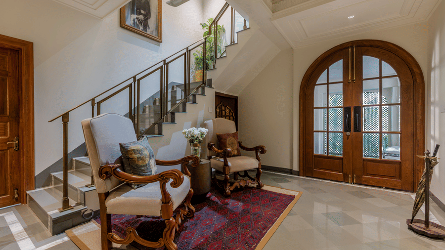 Heritage interior staircase with a wooden arched door, a patterned rug, and natural light at Barwara Kothi, Jaipur.