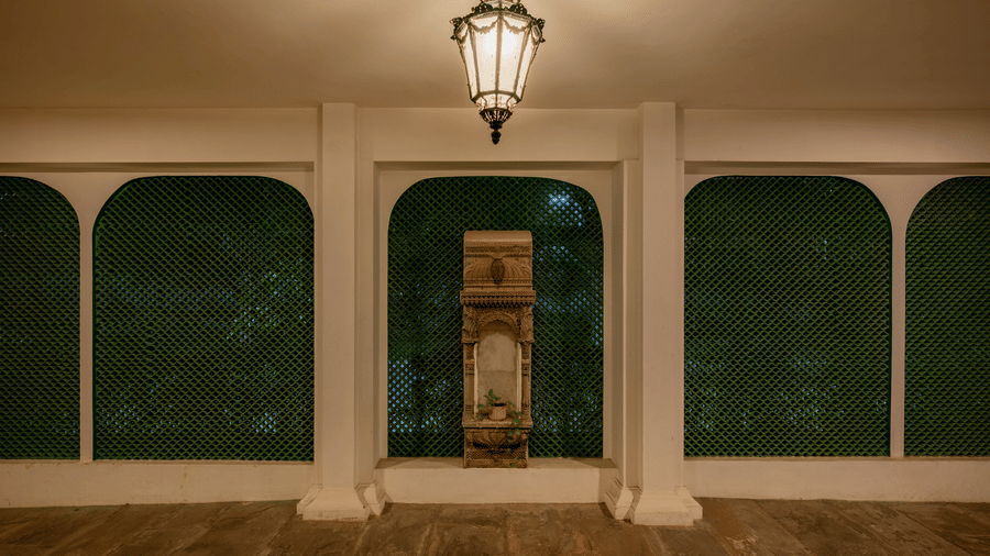 Covered verandah with green-painted arches, a hanging lantern, and a wooden bench along dark wood flooring at Barwara Kotha, Jaipur.