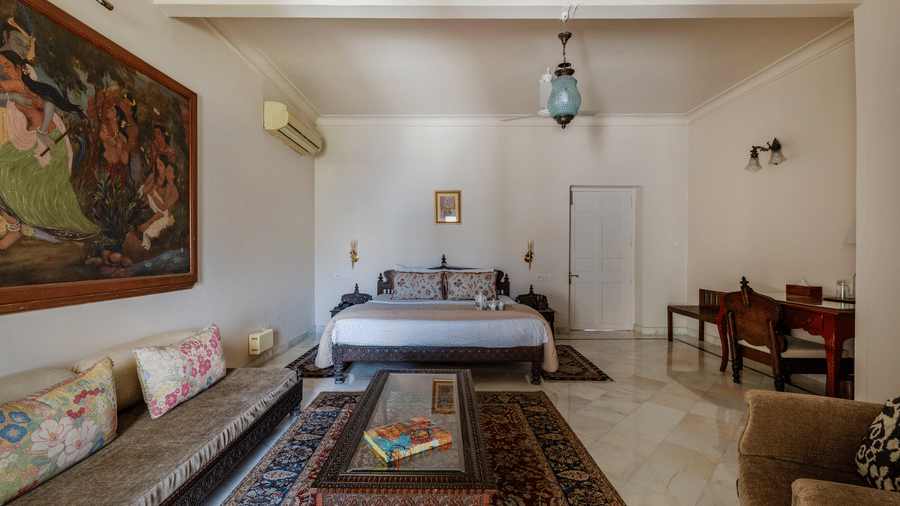 Living room with a sofa, coffee table, arched doorways, decorative wall art, and a ceiling fan at Barwara Kothi, Jaipur.
