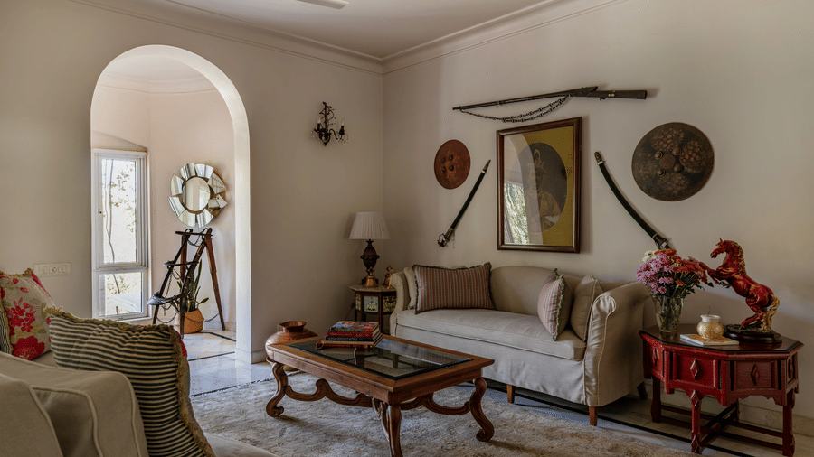 Living room with a sofa, coffee table, arched doorways, decorative wall art, and a ceiling fan at Barwara Kothi, Jaipur.