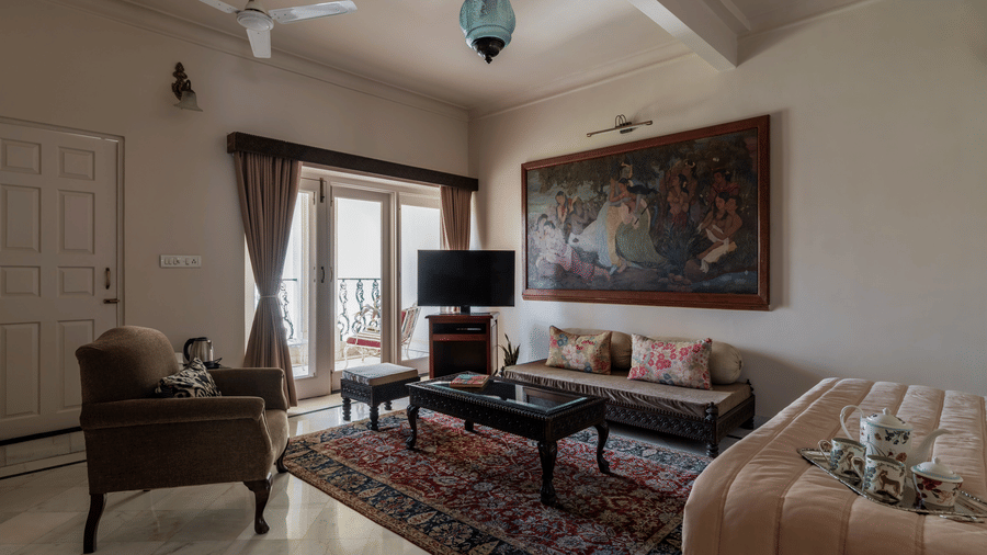 Living room with a large wall mural, sofa, armchair, patterned rug, and draped windows at Barwara Kothi, Jaipur.