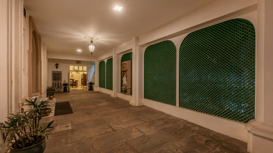 Long corridor lined with green mosaic-tiled arches, potted plants, and warm pendant lighting at Barwara Kotha, Jaipur.