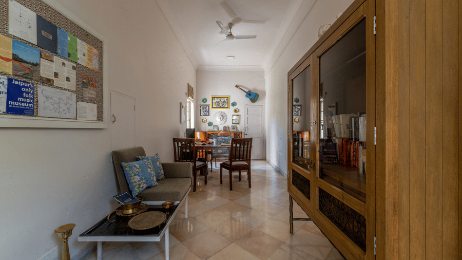 Corridor with striped flooring, a dining table with chairs, and a wooden cabinet along the wall at Barwara Kotha, Jaipur.