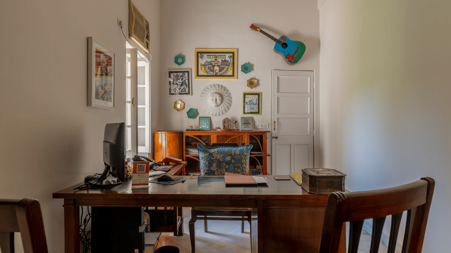 A study room with a wooden desk and chair, decorated walls, and a guitar hanging in the corner.