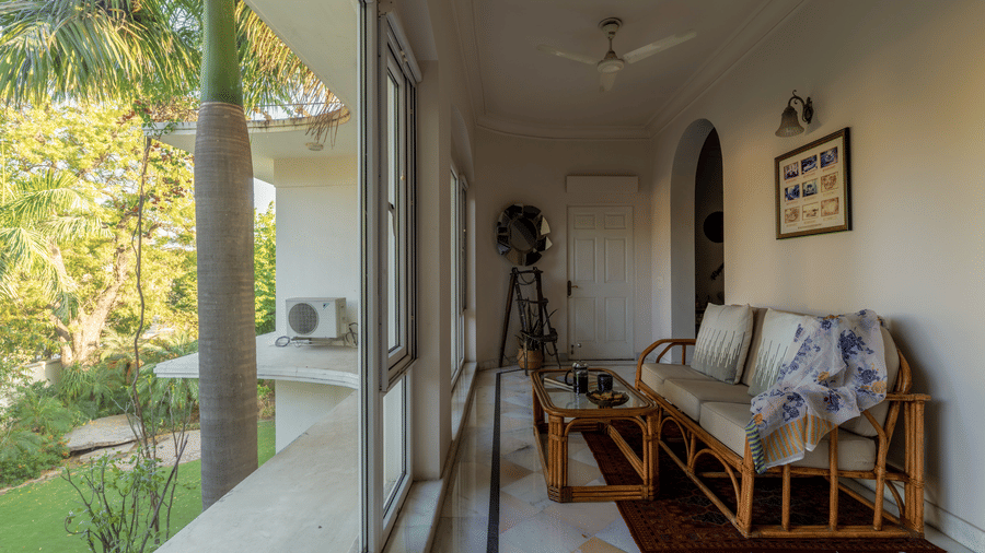 Veranda corridor with a sofa, camera equipment, and glass doors opening to a lush garden at Barwara Kothi, Jaipur.