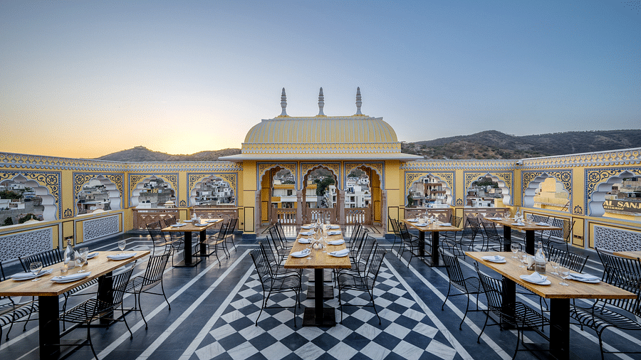 full view image of our roof top dining area with sell set tables and chairs along with a beautiful sunset in the background - Brij Castle, Jaipur