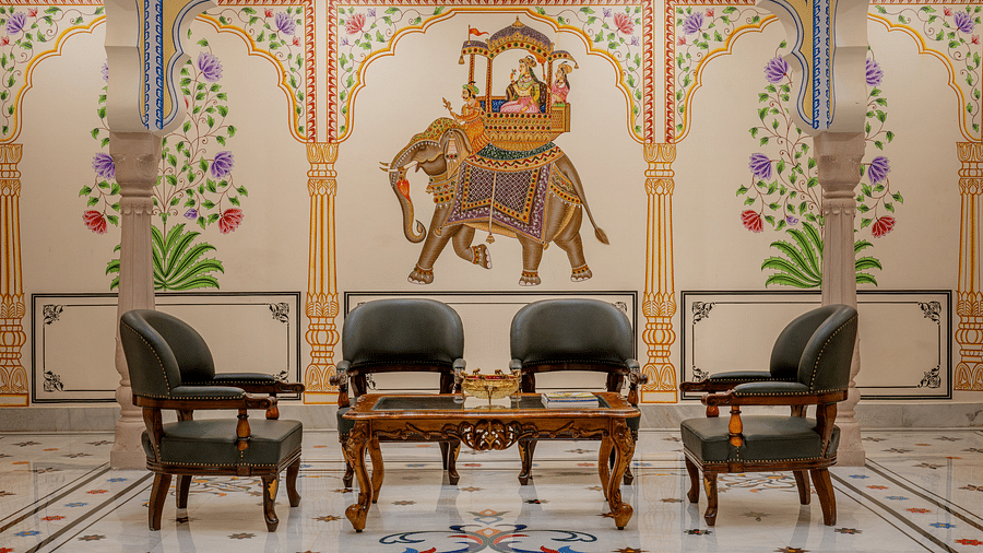 four leather arm chairs placed in front of a beautiful wall with a painting of an elephant carrying a palanquin - Brij Castle, Jaipur