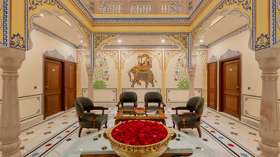 a huge golden vessel filled with bright red rose petals with four arm chairs kept behind it in the the beautiful lobby area - Brij Castle, Jaipur