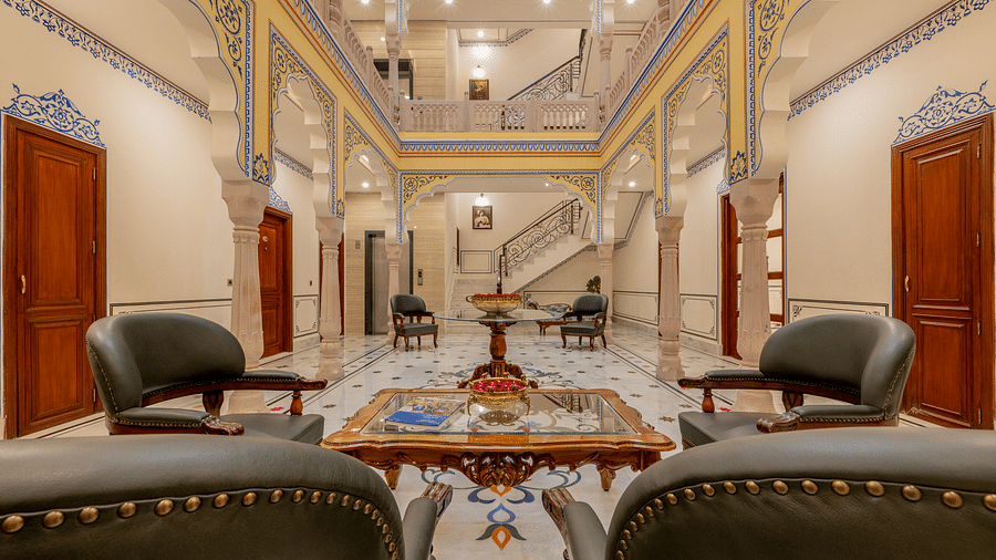an expansive brightly lit lobby area with a common seating area with four leather chairs surrounding a square table top - Brij Castle, Jaipur