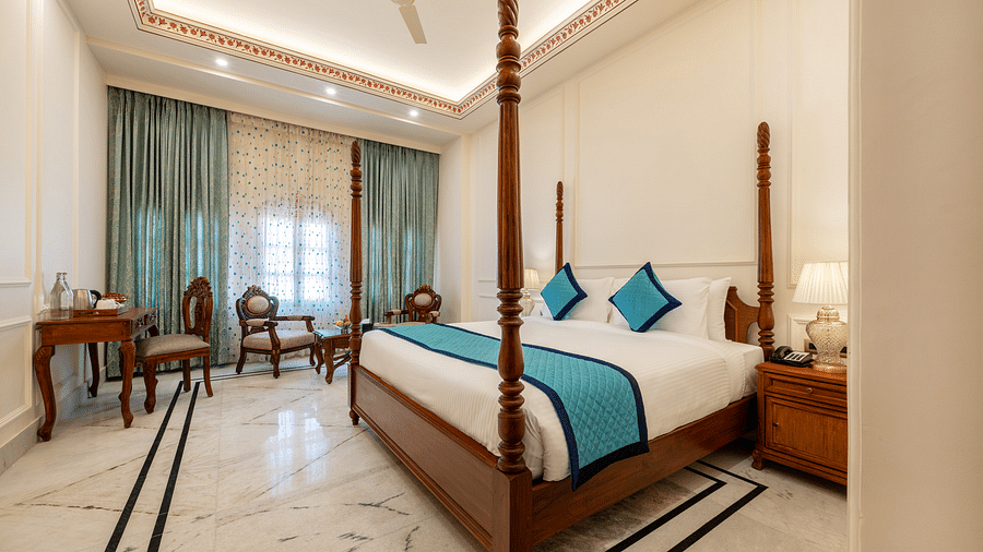 full view image of a room featuring a regal double bed with blue cushions kept over it - Brij Castle, Jaipur