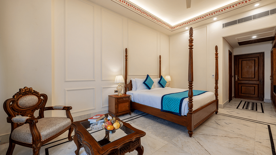 an arm chair with a coffee table in front of it featuring a bowl of fruits along with a plush king size bed behind it - Brij Castle, Jaipur