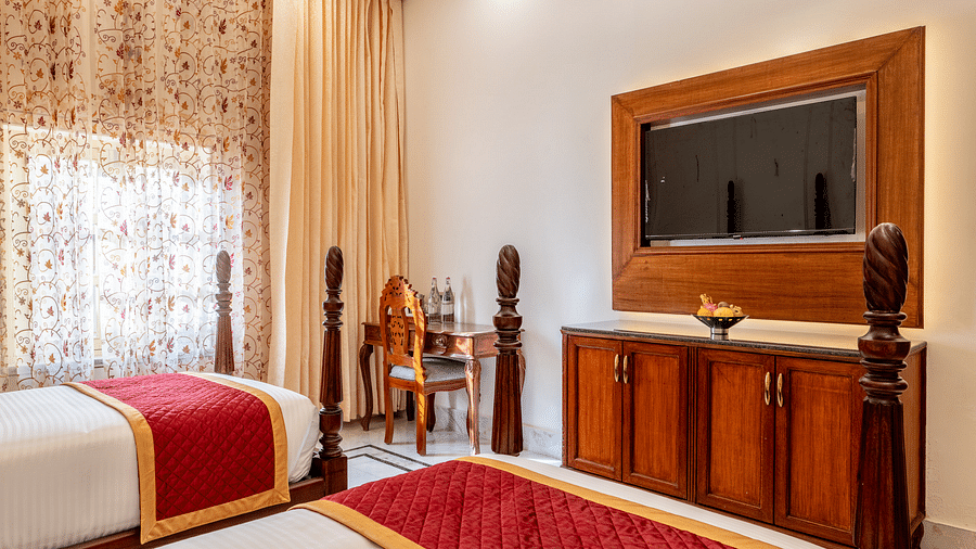 a room featuring a wall mounted television with a work desk and chair in the corner with natural light coming in from the window - Brij Castle, Jaipur