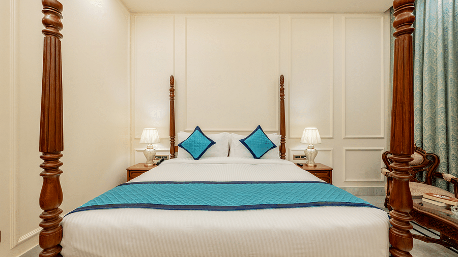 full view image of a king size bed with four wooden pillars at each corner of the bed with blue coloured cushions kept on the bed - Brij Castle, Jaipur