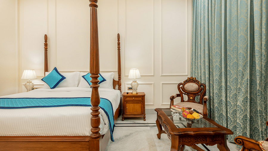 a bedroom with a double bed and a common seating area with a glass top centre table with a fruit bowl in the table - Brij Castle, Jaipur