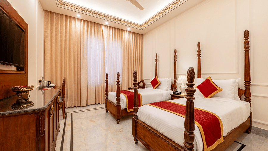 a brightly lit room featuring a twin bed with red coloured cushions - Brij Castle, Jaipur