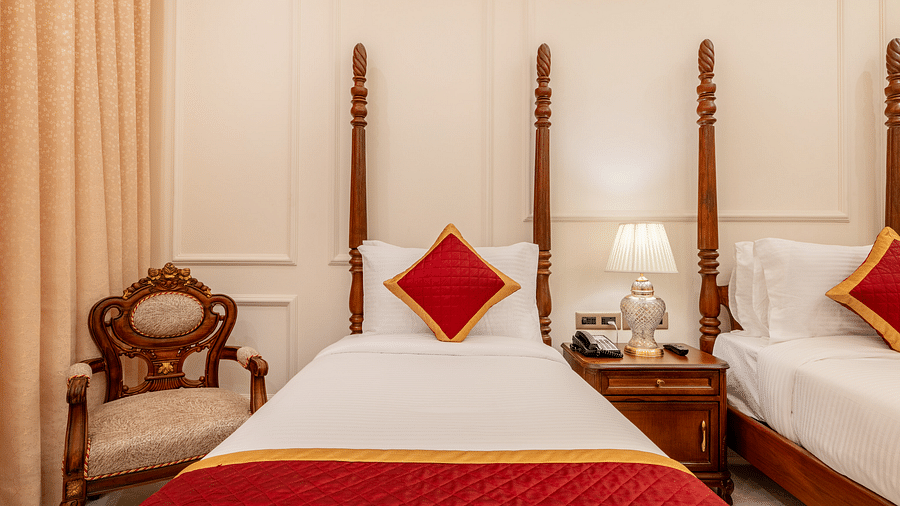 a single bed with a red cushion set against the headboard and an armchair besides it - Brij Castle, Jaipur
