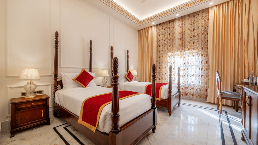Twin poster beds with red accents, wooden nightstand, and study desk in a elegant bedroom at Brij Castle.