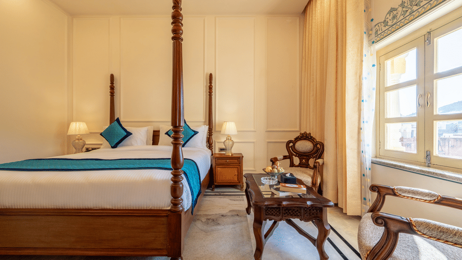A poster bed with a turquoise runner, nightstands, and seating area near a window in a bedroom at Brij Castle.
