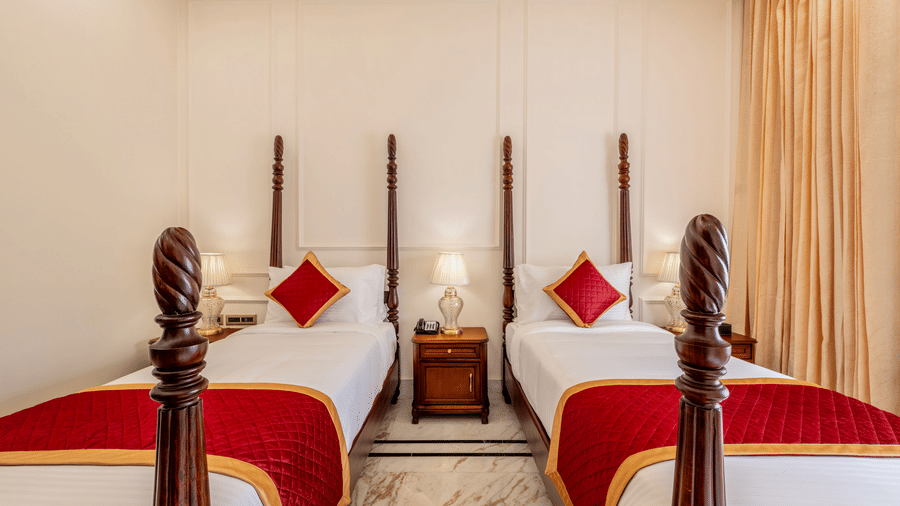 A bedroom with twin poster beds, red cushions, wooden nightstand, and soft lighting at Brij Castle.