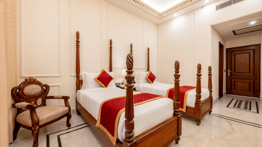 Twin poster beds with red runners alongside a carved wooden armchair in a bedroom at Brij Castle.