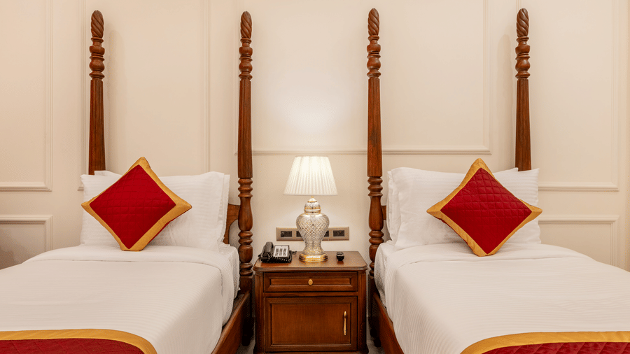 Twin poster beds with red cushions and white sheets flanking a nightstand in a bedroom at Brij Castle.