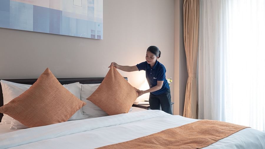 A staff member making a bed, adjusting pillows on a large white bed with orange decorative pillows and a matching bed runner | Central Mansions, Phnom Penh