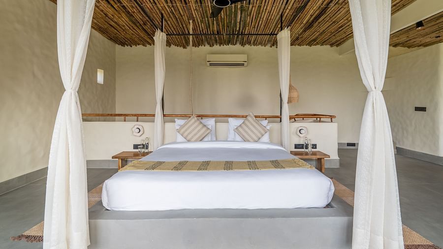 Front view of a four-poster bed with flowing white curtains and rustic wooden ceiling.