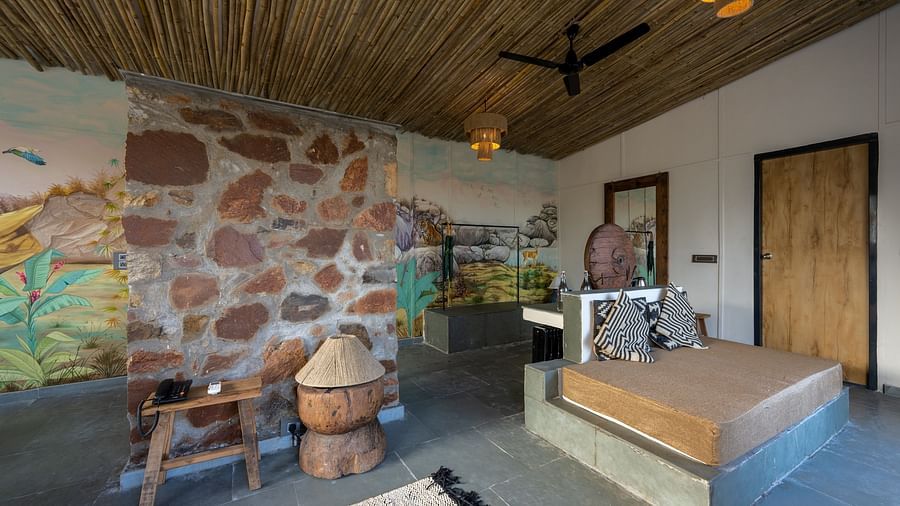 An image of a room with a queen size bed, chandeliers, ceiling fan, decorative items, and wall paintings - Utsav Camp Sariska