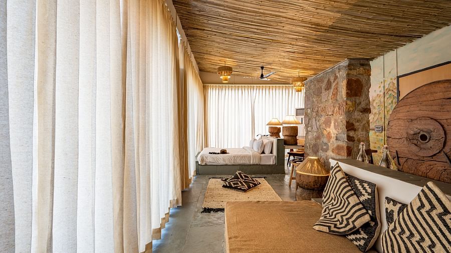 An image of a room with a queen size bed, a couch, ceiling fan, chandeliers, decorative items, and wall paintings - Utsav Camp Sariska