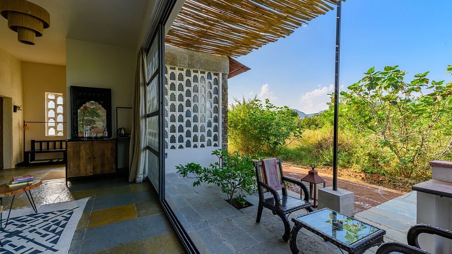 An image of a room with a chandelier, and other decorative items and an expansive glass door over viewing the green landscape - Utsav Camp Sariska