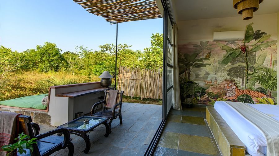 An image of a room with a queen size bed and decorative items with wall hangings and an expansive glass door with an outdoor seating arrangement - Utsav Camp Sariska